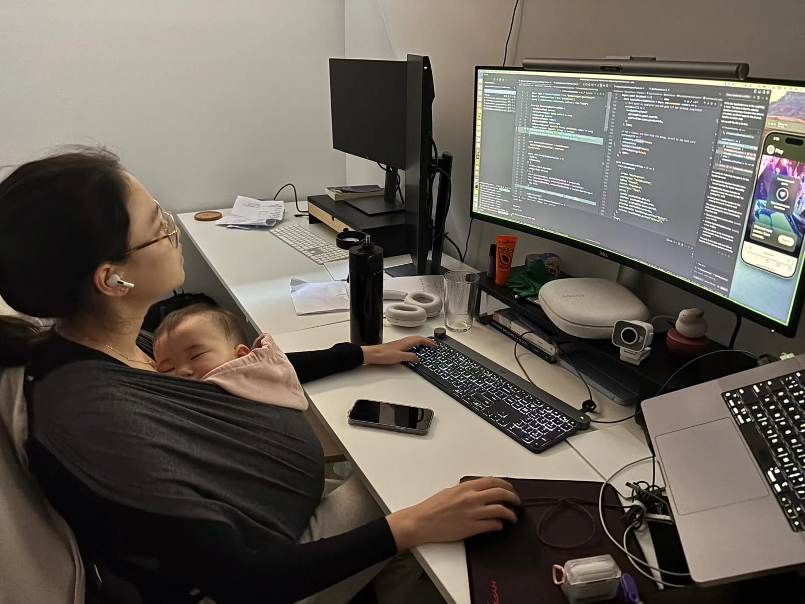 Sharon Sheah working on software at her desk with her baby in a carrier